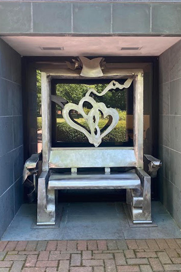 stainless steel bench for two people featuring a tall back that frames two steel hearts intertwined